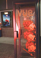 Image of Vue cinema internal glass door with red-haired triplet appearing to peep around it, an a poster of Brave in the background showing Merida.